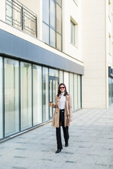 Obraz premium Beautiful brunette young woman in nice brown beige coat and sunglasses on urban background.
