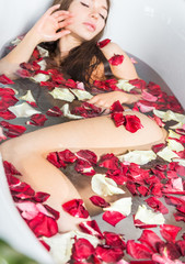 Obraz na płótnie Canvas A young attractive girl takes a bathroom with flower petals and relaxes against the background of a beautiful light interior. Spa treatments for beauty and health with skin care