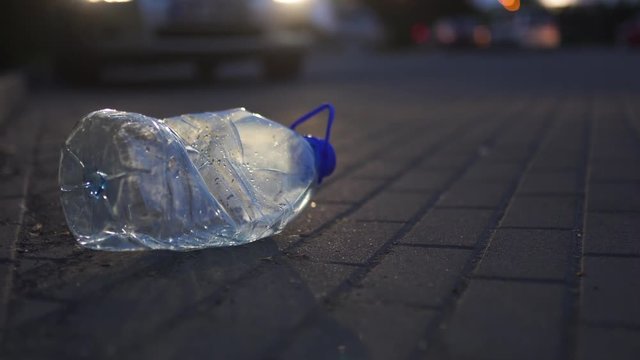 Plastic bottle lying on the ground at night in front of a car - Thrown out not recycled - Trash and pollution of the city and nature - Decayed rubbish