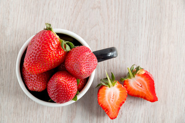 Fresh ripe strawberries in black metal cup on wooden background flat lay