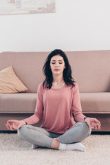 Fototapeta premium beautiful woman with eyes closed in Lotus Pose practicing meditation in Living Room at home