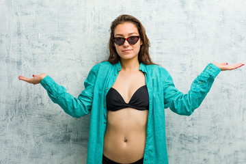 Young european woman wearing bikini doubting and shrugging her shoulders in questioning gesture.
