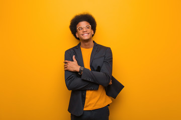 Young business african american man over an orange wall smiling confident and crossing arms,...