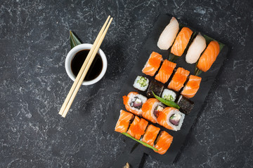 Various kinds of sushi rolls served on black stone background.