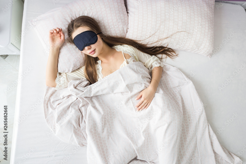 Wall mural Beautiful young girl sleeping in the morning in her bed with a face mask. View from above