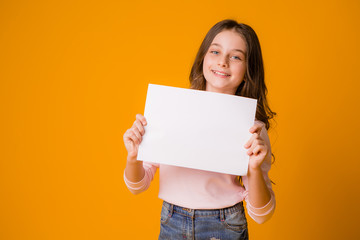 Naklejka na ściany i meble baby girl smiling holding a blank sheet on a yellow background. space for text