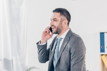 handsome smiling businessman in suit talking on smartphone in office with copy space