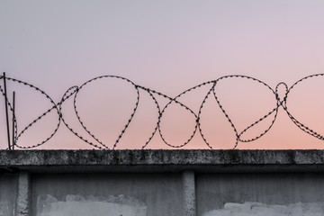 concrete wall with barbed wire against a blue orange evening sky