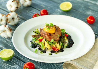 Beef cutlet with mashed potatoes, garnished with microgreens, tomatoes, egg yolk and black sauce