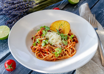 Classic Italian Bolognese pasta, decorated with microgreen, grated parmesan and a slice of dry orange on the table on a sunny day, on a plate