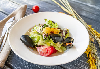 Salad with mussels, lettuce and tomatoes, garnished with microgreen and a slice of grilled lemon