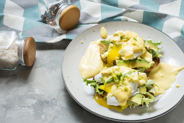 Eggs Benedict with avocado on concrete background.