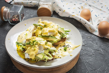 Eggs Benedict with salad and avocado on stone background.
