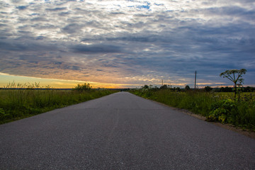 Road in the field at sunset. Summer field. Asphalt road. Summer landscape. Russian roads.