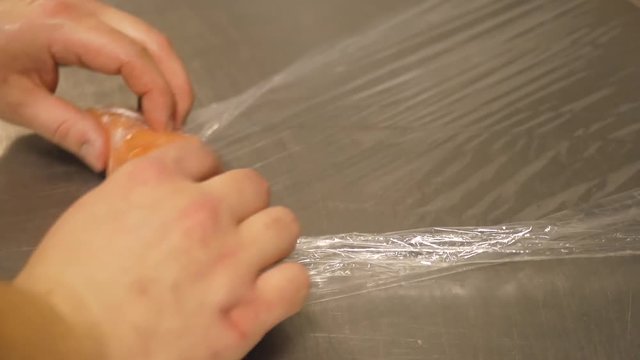 Human hands take a piece of sliced salmon fillet and wrap it in pey film. Preparing fish for freezing. Close-up.