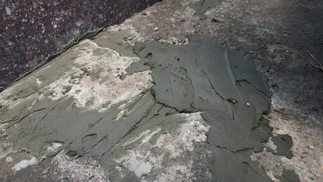 Hand with putty knife repair cracks with cement in the floor at the cemetery. Slow motion