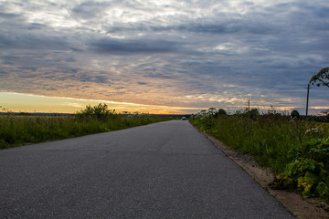 Road in the field at sunset. Summer field. Asphalt road. Summer landscape. Russian roads.