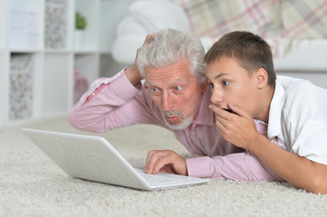 Grandfather with grandson using laptop while lying on floor 