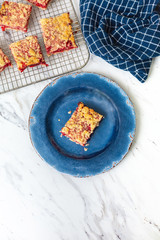 Freshly Baked Strawberry Bar Cookies cooling on a wire rack, one isolated in front on blue plate, blue kitchen towel, white countertop