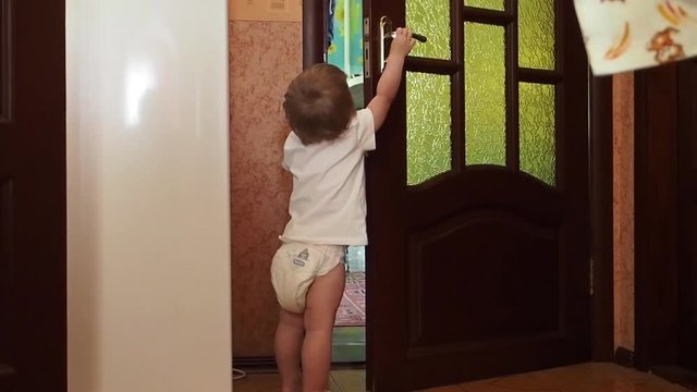 Cute little boy in the house opens the door  Blond baby dressed in a diaper and a t-shirt is played opening the door