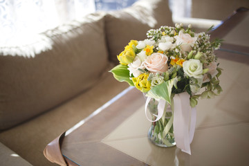 A bright wedding bouquet of spring flowers is in a glass vase on a table in a restaurant.