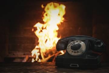 Black old phone on a table on a burning fire in fireplace background. Hotline concept.