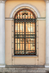 A window with an arch and a lattice with peaks on a yellow wall between two white columns. Old European architecture