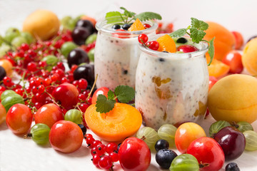 Fresh yogurt with chia seeds. Currants, cherries, gooseberries, apricots and blueberries on a white table.