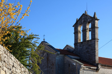 Fototapeta na wymiar Church with bell tower in Pula view in spring time with blooming forsythia.