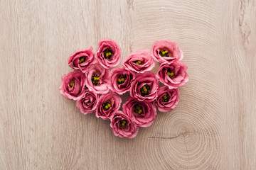 top view of heart sign made of pink eustoma flowers on wooden table