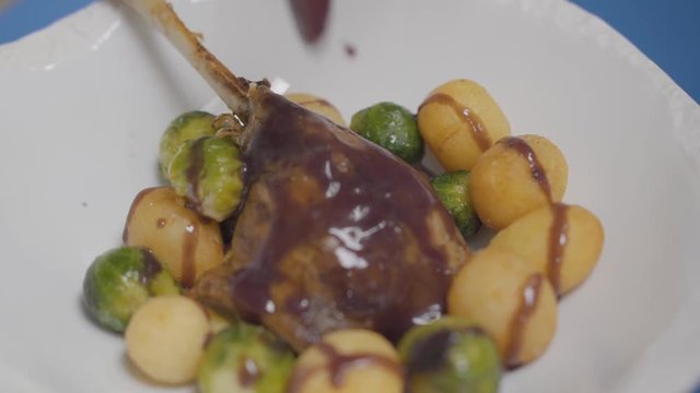 White plate with duck leg, potato balls and brussels sprouts on the sause
