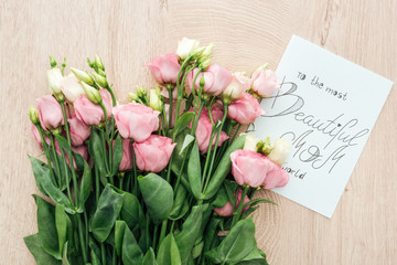 top view of pink eustoma flowers and card with to the most beautiful mom in the world lettering on wooden table