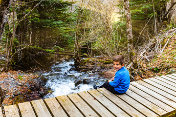 Kid sitting on a bridge with a river background