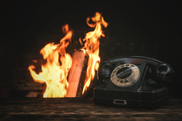 Black old phone on a table on a burning fire in fireplace background. Hotline concept.