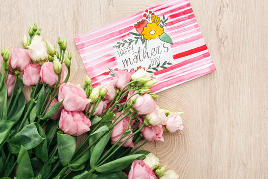top view of eustoma flowers and card with happy mothers day greeting on wooden surface