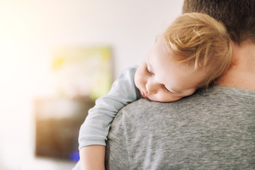 Close-up portrait of cute adorable blond caucasian toddler boy sleeping on fathers shoulder...