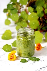 Pesto nasturtium leaves in a glass jar on a background of nasturtium foliage. dishes with nasturtium, edible flowers and herbs.