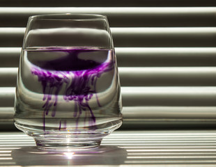 diffusion of blue ink in a transparent glass cup with clear water against the background of a...