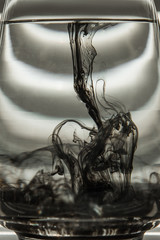 a cloud of ink in a transparent glass cup with clear water against the backdrop of a striped screen with rays of light. Template, layout, background, texture. macro diffusion black and white