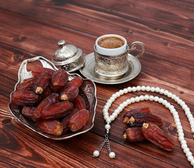 Islamic festival of Ramadan concept. Delicious tropical dates on a silver plate with rosary beads and Turkish coffee on a brown wooden table background. Traditional Middle East culture. Ramadan Kareem