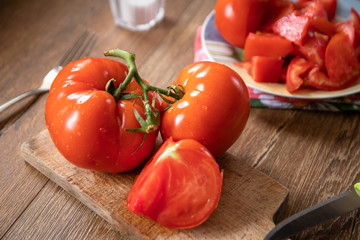 Whole and sliced tomatoes on cutting board and ceramic plate on old wooden table