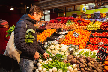 Handsome young men holding eco shopping bag while standing in a food market. Man choosing vegetables