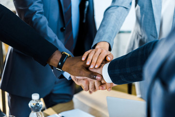 Obraz premium cropped view of multicultural men and businesswomen putting hands together