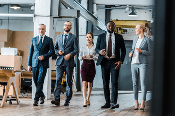 multicultural group of handsome businessmen and cheerful businesswomen walking in office