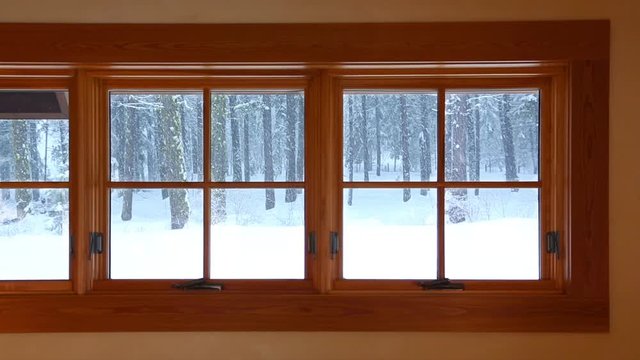 View from home interior wood windows of snow falling outside. Cozy, warm house in cold winter weather hd video.