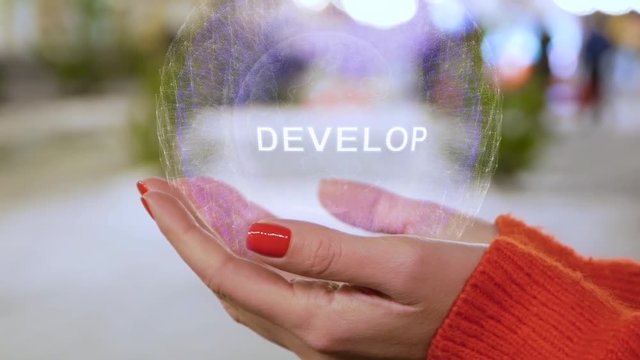 Female hands holding a conceptual hologram with text Develop. Woman with red nails and sweater with future holographic technology on a blurred background of the street