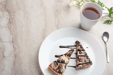 On the plate are two slices of cheesecake with tea and flowers, with space for congratulations