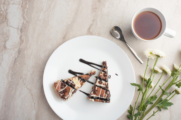 On the plate are two slices of cheesecake with tea and flowers, with space for congratulations