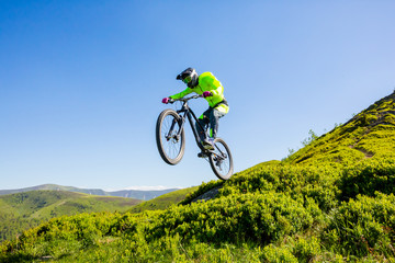Professional bicycle rider is jumping on the mountain trail.