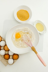 Baking ingredients closeup. Eggs sugar and oil on the table. Flour, egg and milk in a bowl with a whisk. Flat lay view.